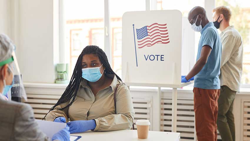 Masked woman checking in citizen to vote; citizens voting in booth